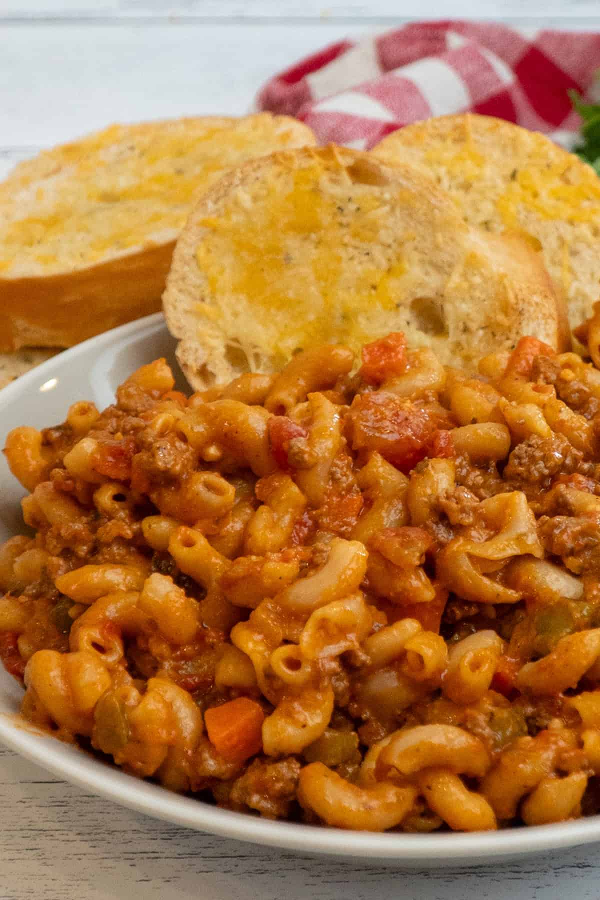 A bowl filled with American-style goulash and some bread on the side of the bowl.