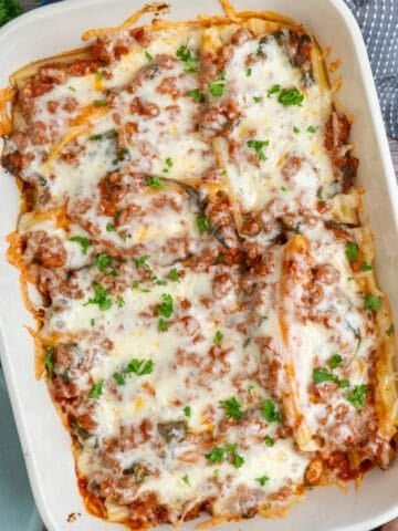 String cheese manicotti in a baking dish and garnished with parsley.