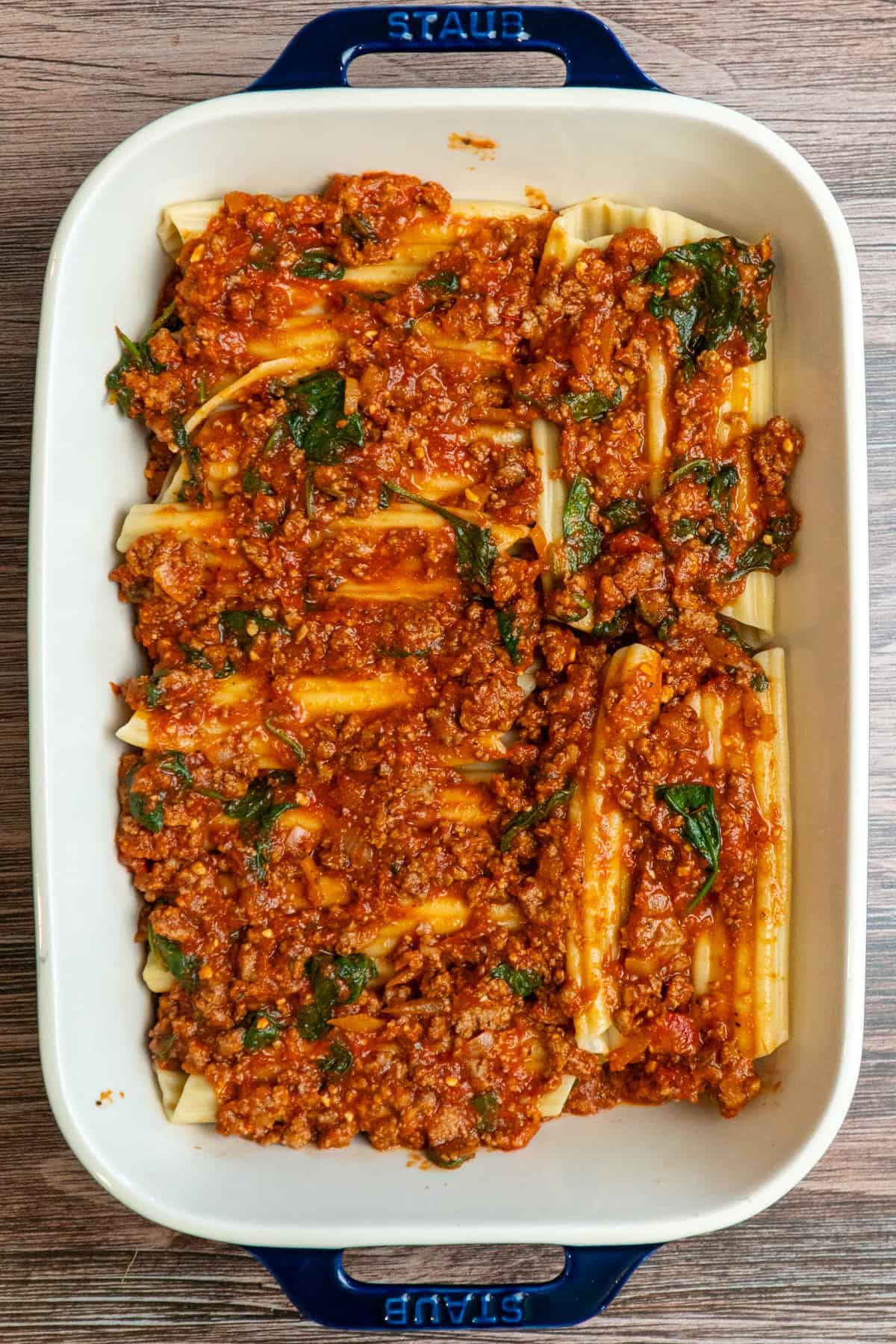 Manicott shells stuffed with string cheese and meat sauce poured over the top in a baking dish.