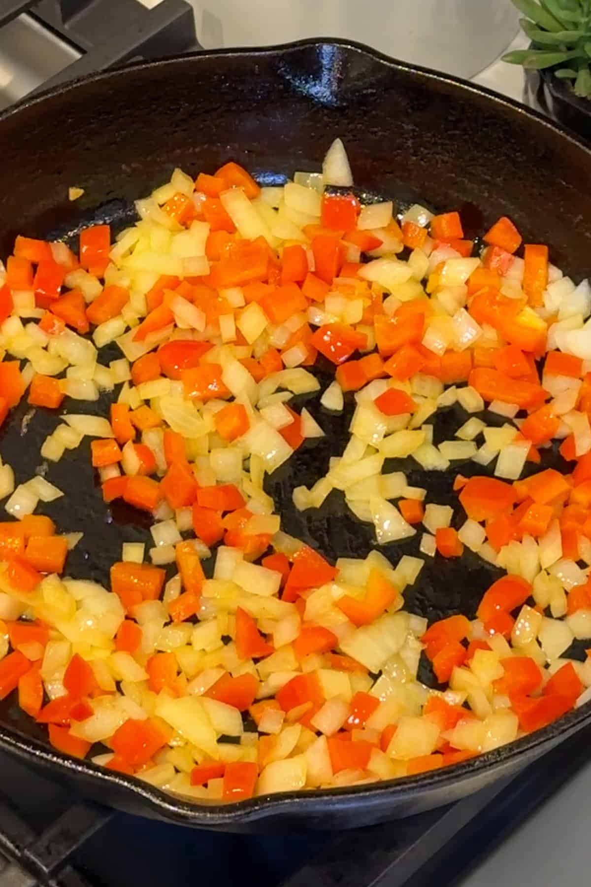 Onions and red bell peppers sauteing in a skillet.