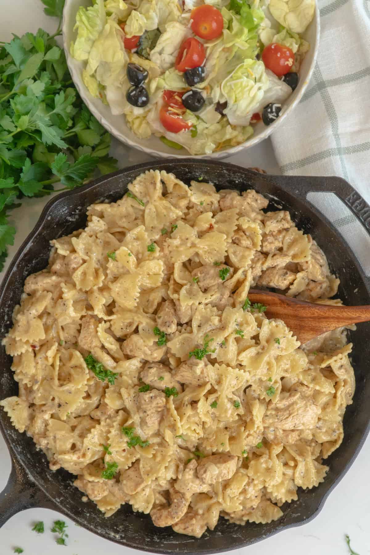 Garlic parmesan pasta chicken in a skillet with a wooden spoon ready to serve.