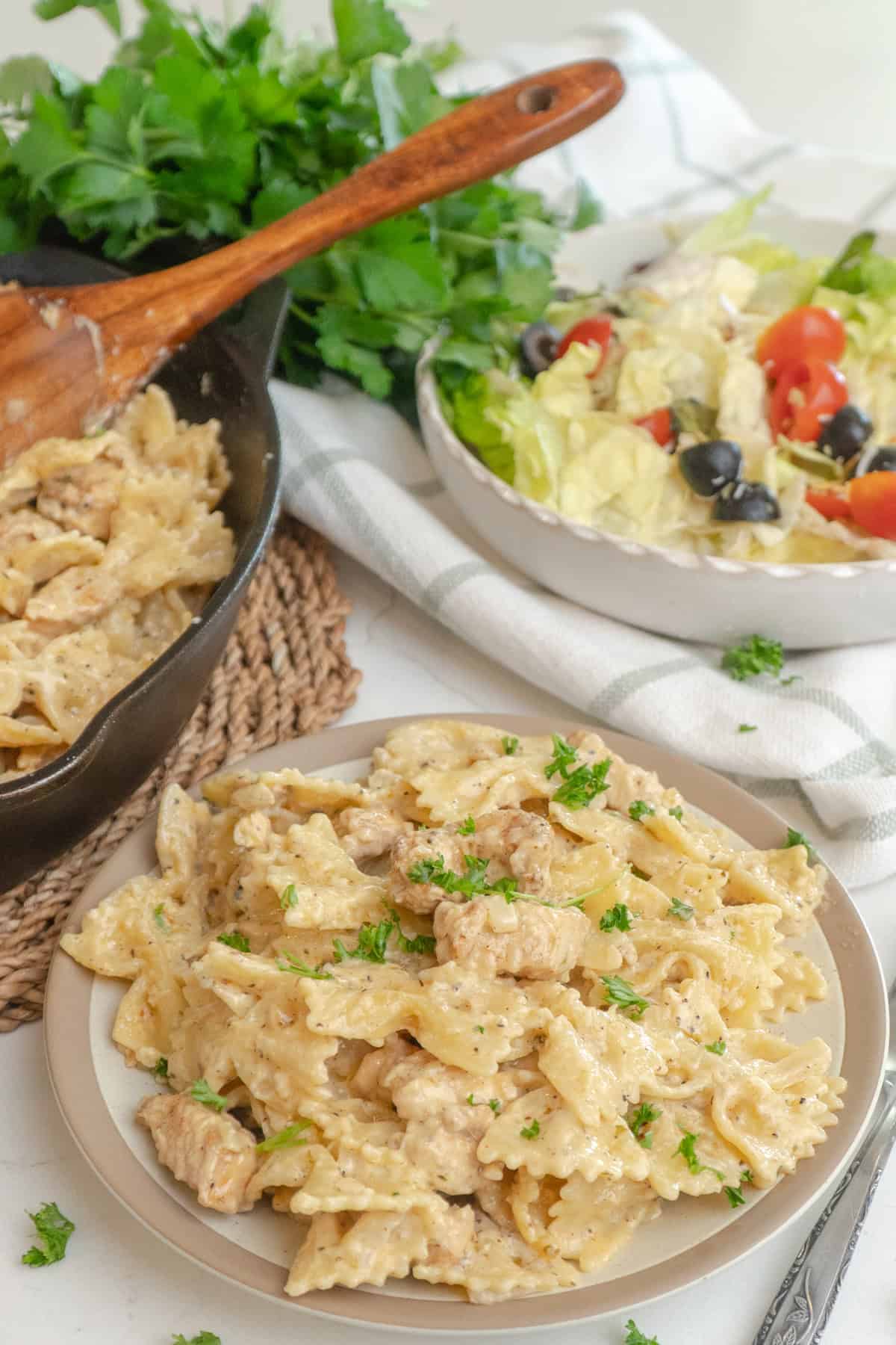 Garlic parmesan pasta with chicken on a plate with a salad in the background.