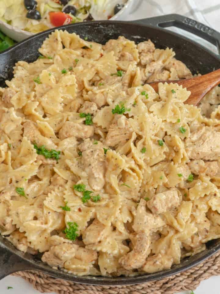 Garlic parmesan pasta chicken in a skillet with a wooden spoon ready to serve.