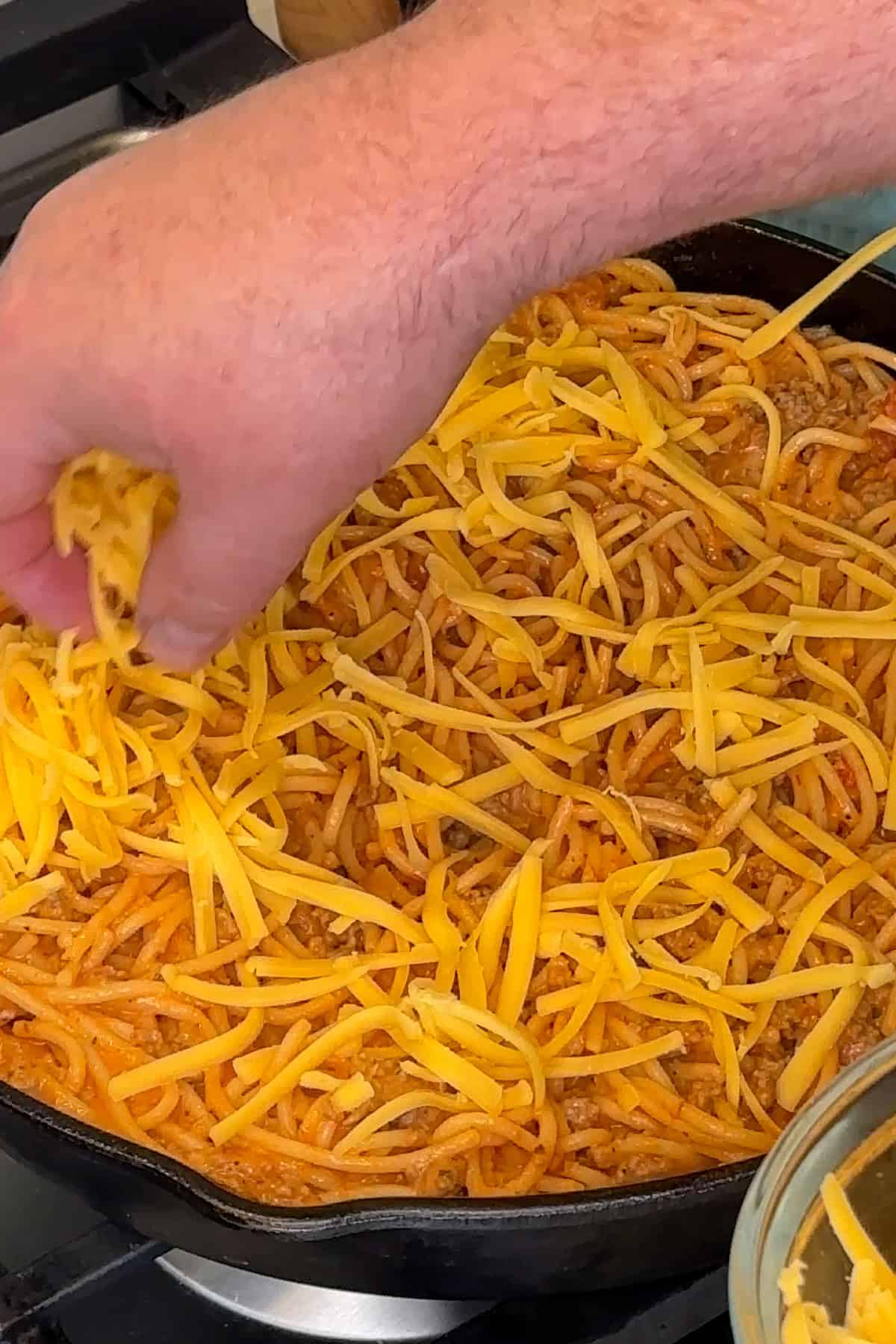 Cooked spaghetti tossed in sauce and topped with grated cheddar cheese.