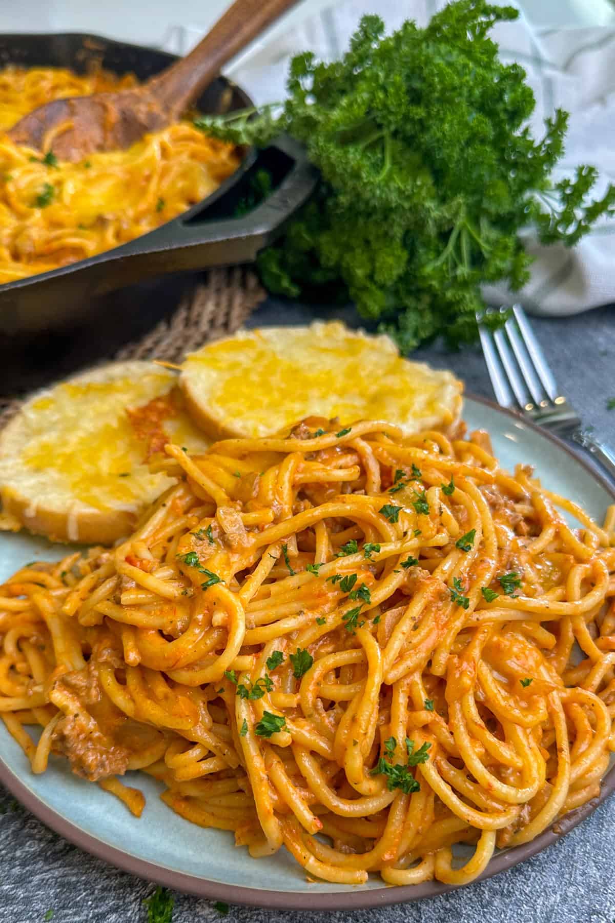 Cheesy baked spaghetti on a plate with two pieces of cheese bread.