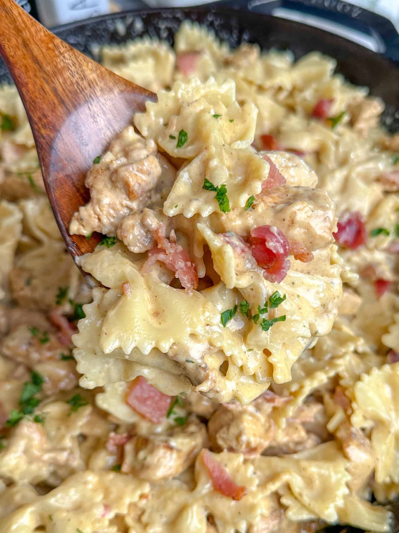 A wooden spoon holding a scoop of chicken bacon ranch pasta over a skillet.