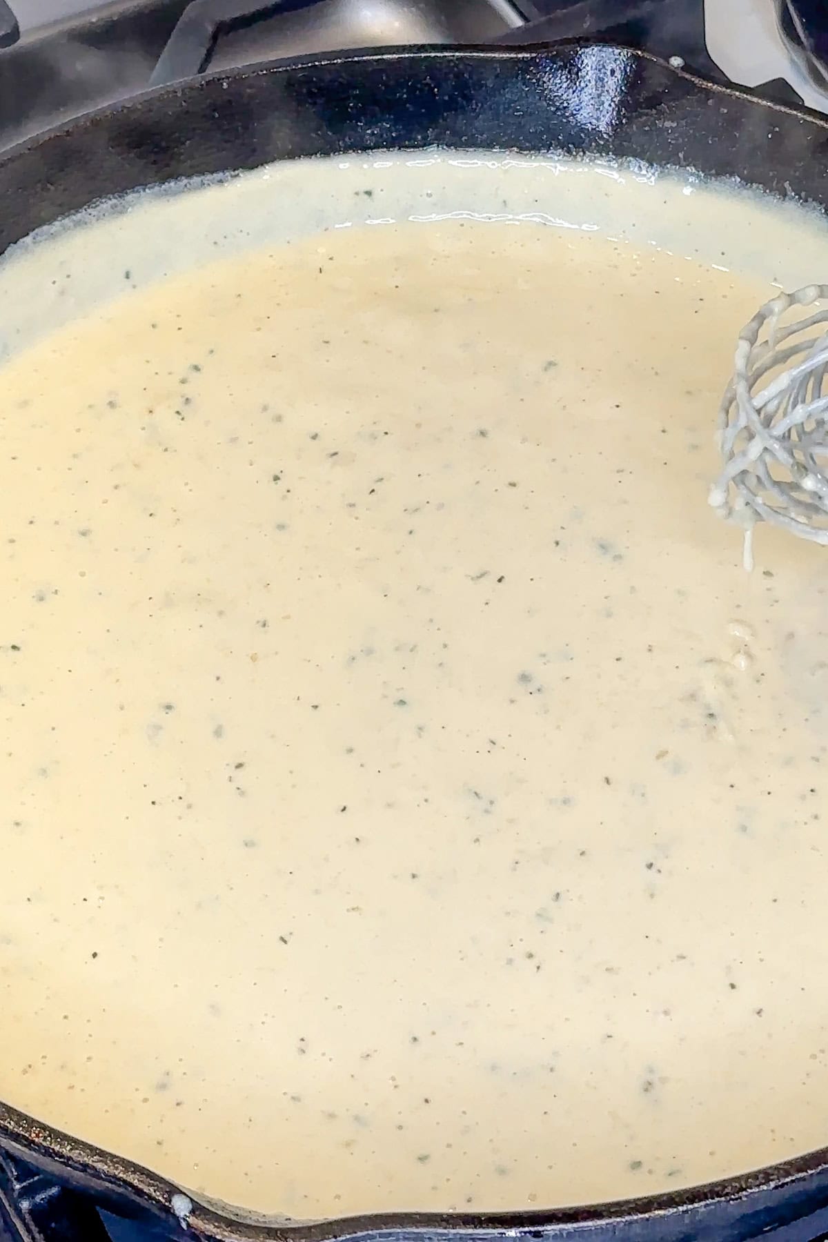 Creamy alfredo ranch sauce being whisked together in a skillet.