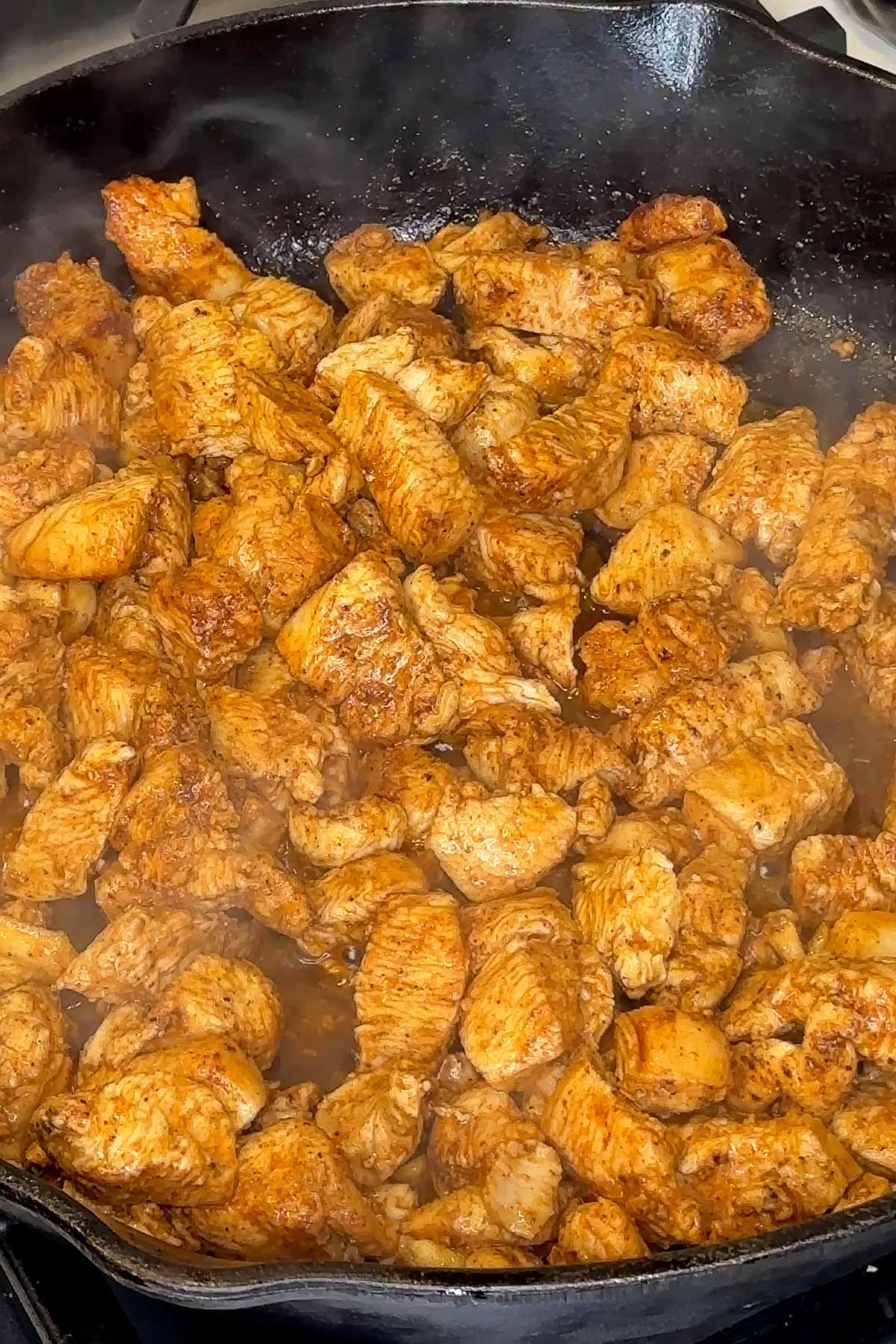 Seasoned chicken being cooked in a skillet.