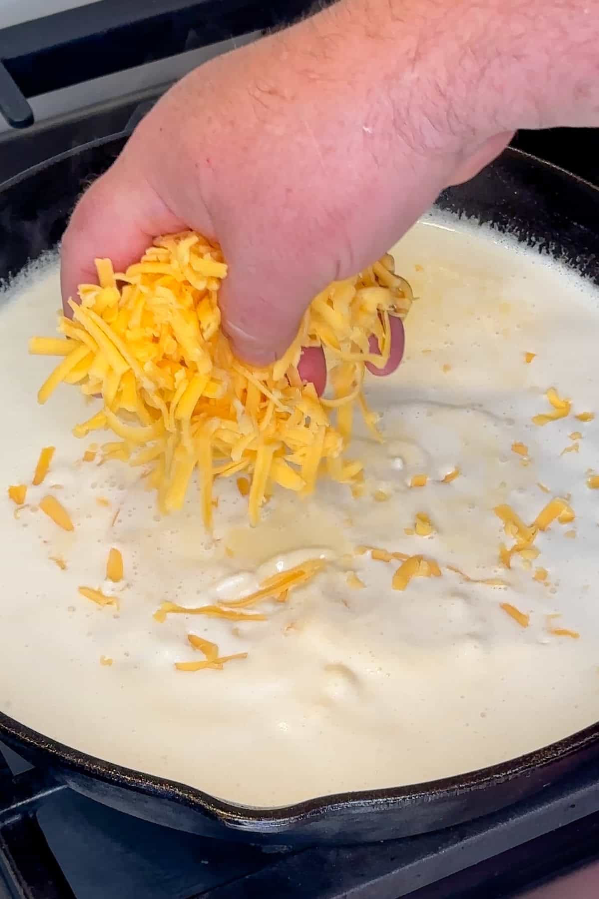 Cheddar cheese being added to sauce base in a skillet.