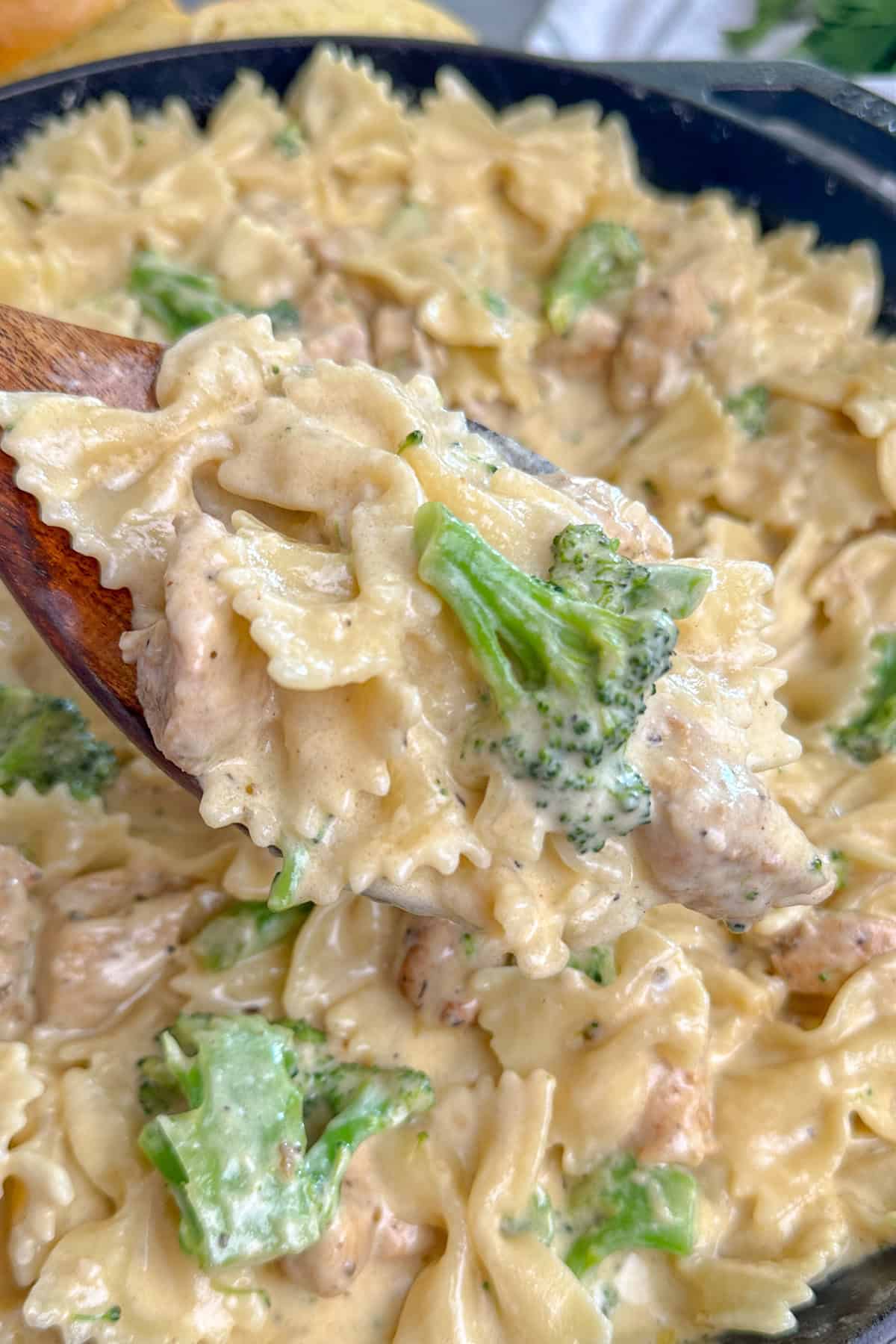 A wooden spoon holding a scoop of chicken broccoli pasta.