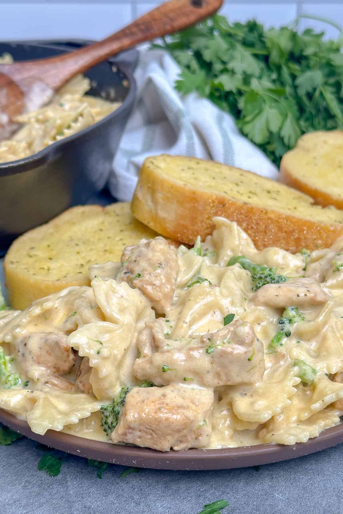 Chicken broccoli pasta on a plate with garlic bread.
