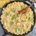 Cheesy chicken broccoli pasta in a skillet with a wooden spoon.