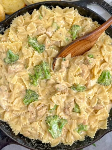 Cheesy chicken broccoli pasta in a skillet with a wooden spoon.