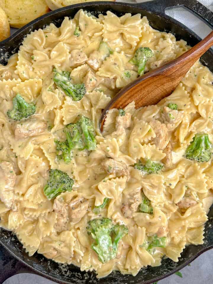 Cheesy chicken broccoli pasta in a skillet with a wooden spoon.