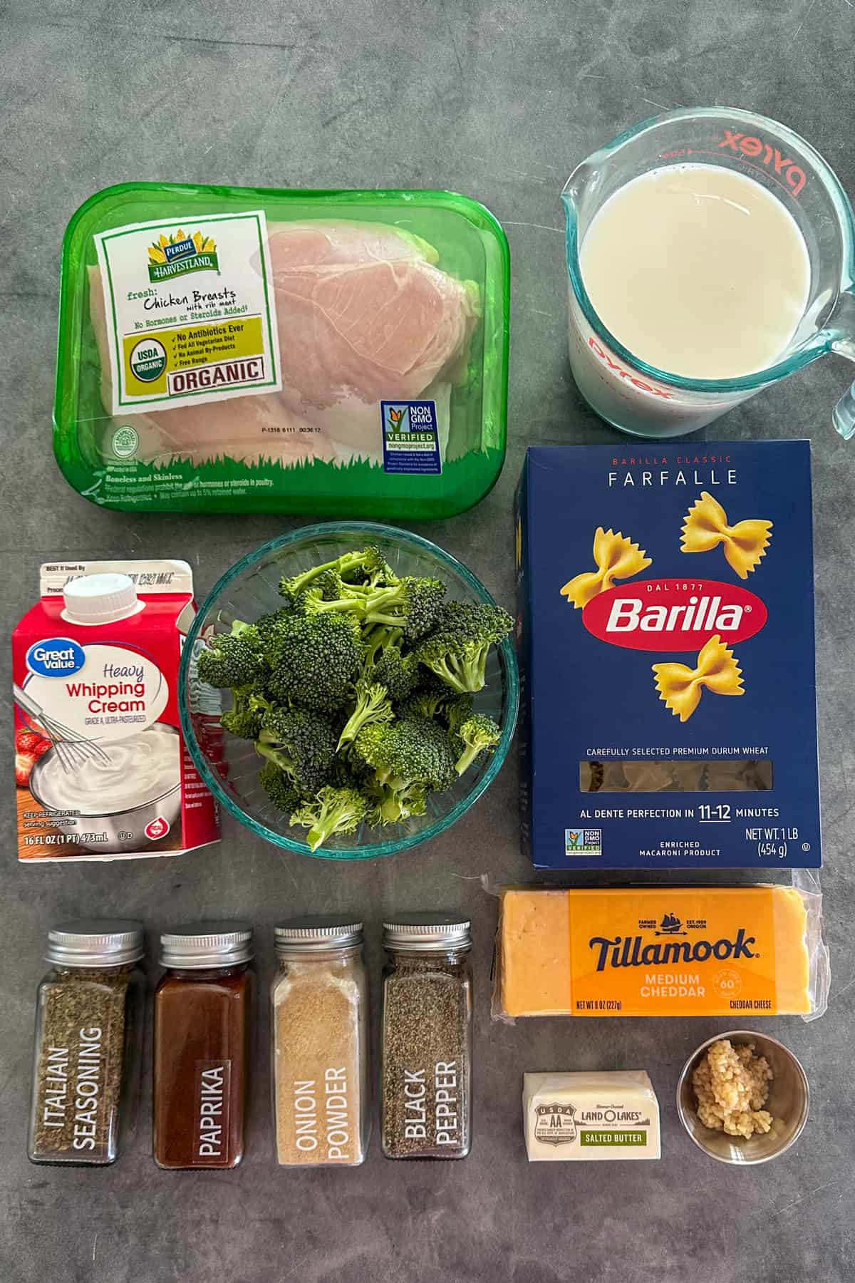 Ingredients to make cheesy chicken broccoli pasta on a gray counter top.