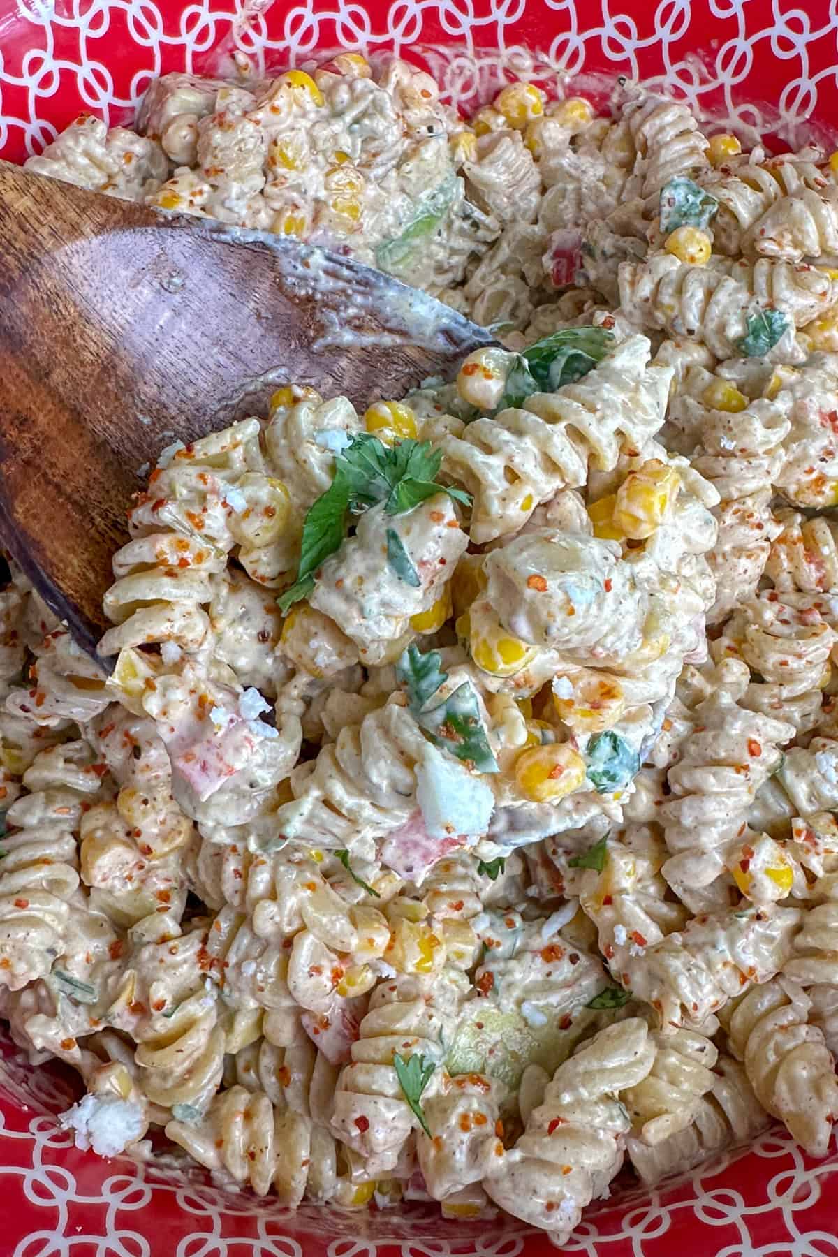 A wooden spoon holding a scoop on street corn pasta salad.