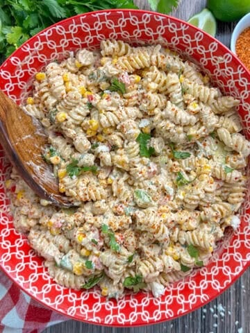 Mexican street corn pasta salad in a colorful bowl with a wooden spoon.
