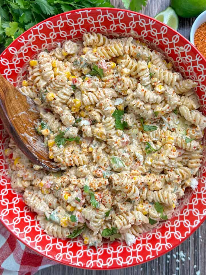 Mexican street corn pasta salad in a colorful bowl with a wooden spoon.
