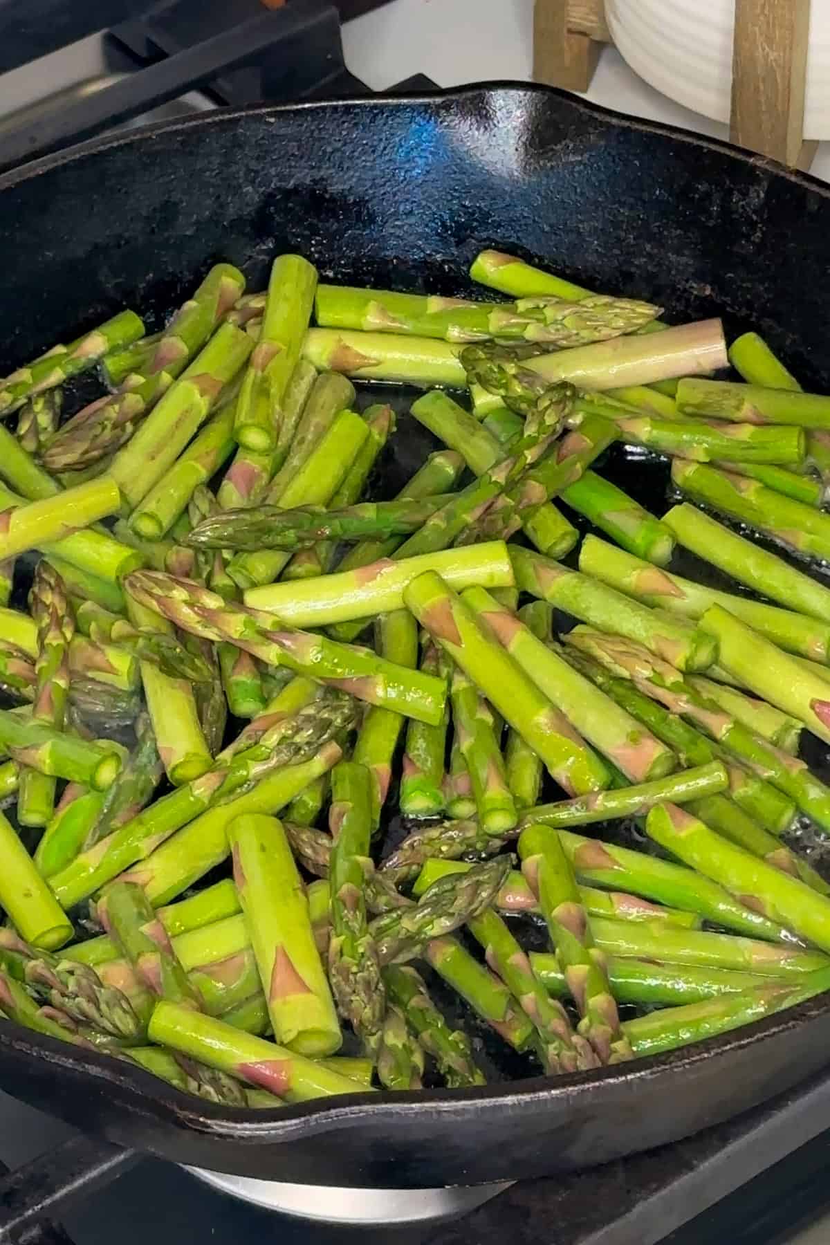 Asparagus pieces cooked in butter in a cast iron skillet.