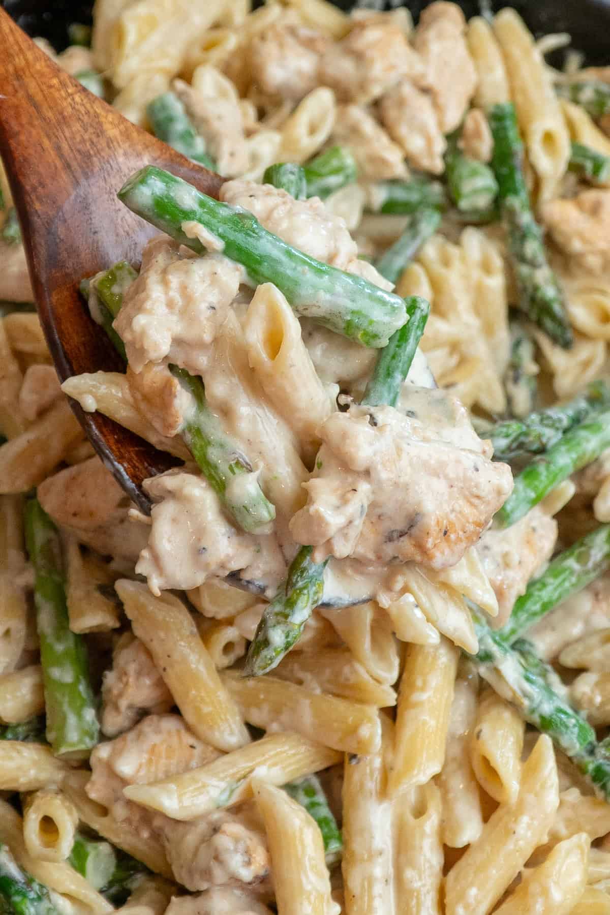 A wooden spoon holding a scoop of chicken asparagus pasta.