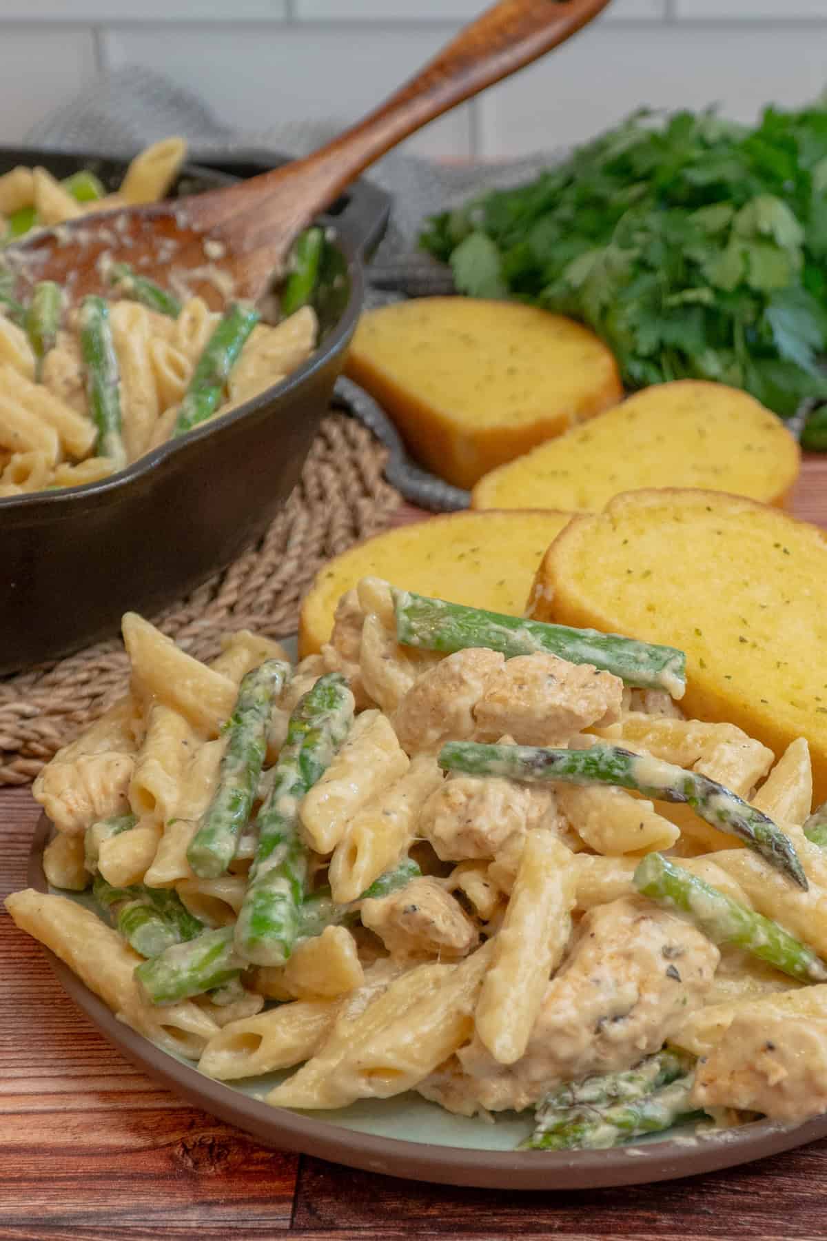 Chicken asparagus pasta on a plate with garlic bread.