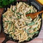 Chicken asparagus pasta in a cast iron skillet with a wooden spoon in it.