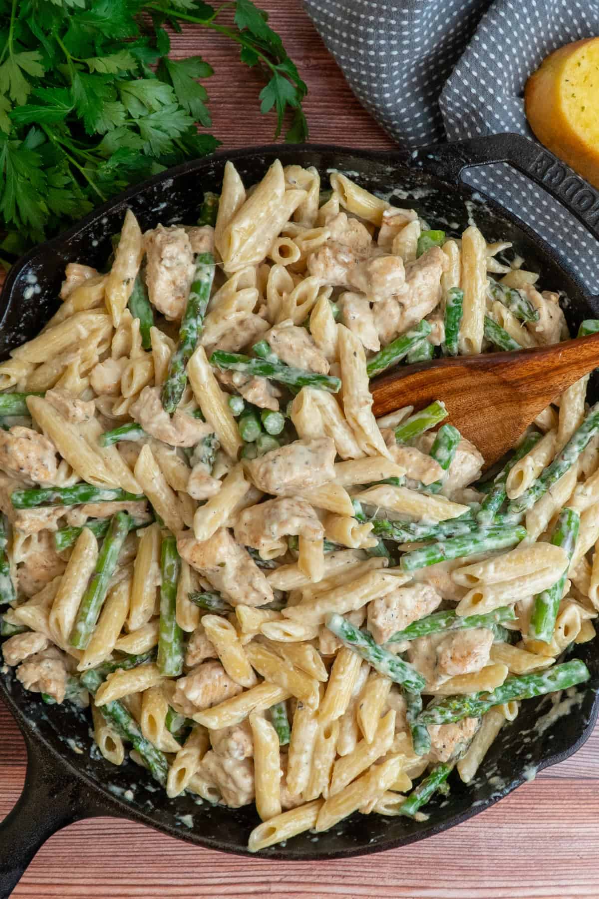 Chicken asparagus pasta in a cast iron skillet with a wooden spoon in it.