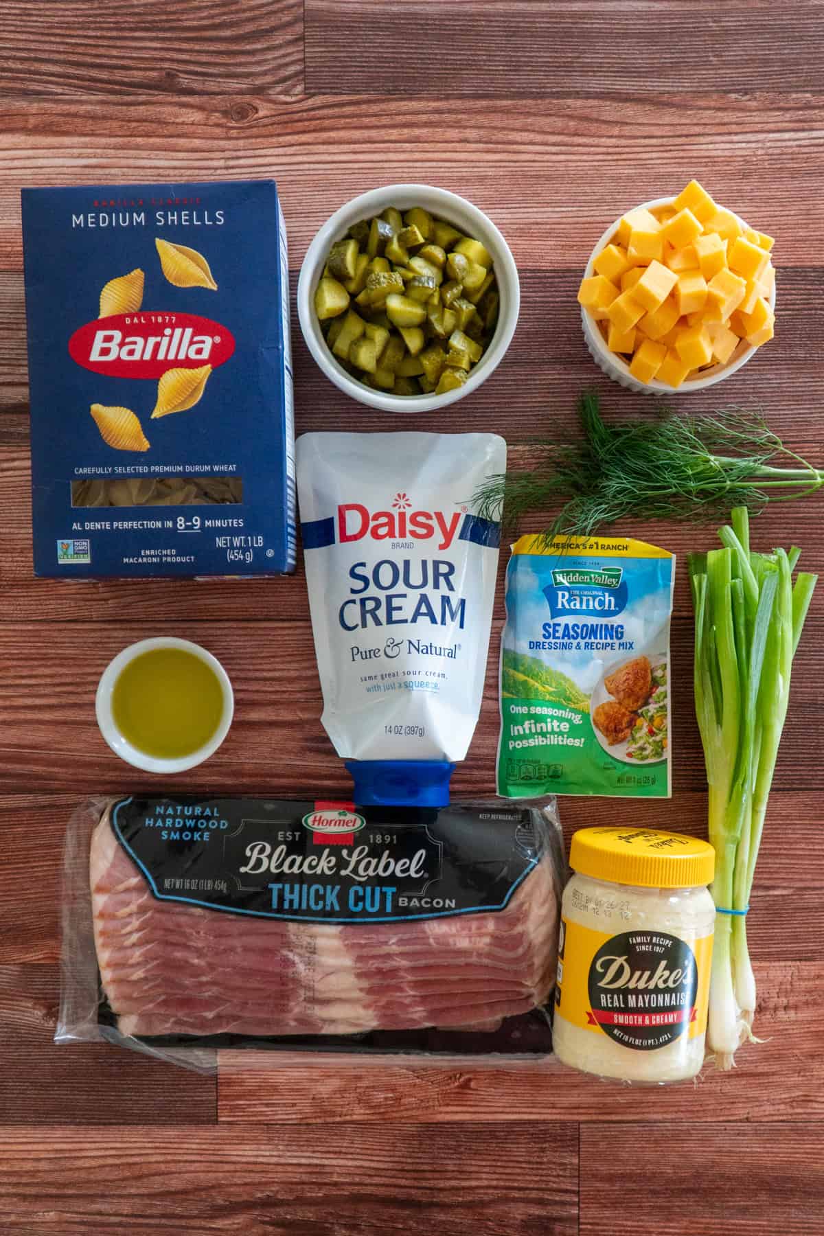 All the ingredients to make dill pickle pasta salad on a wooden countertop.