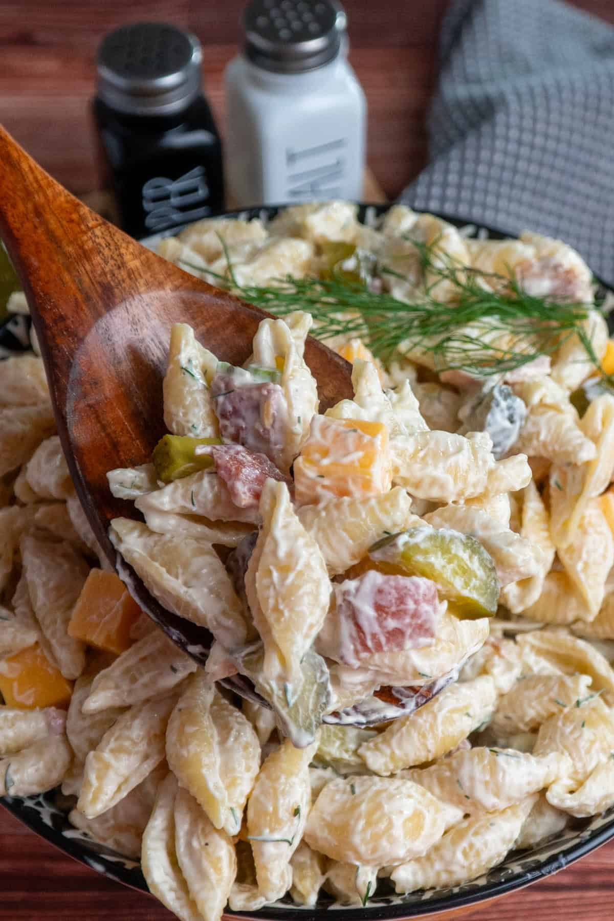 A wooden spoon holding a serving of dill pickle pasta salad.