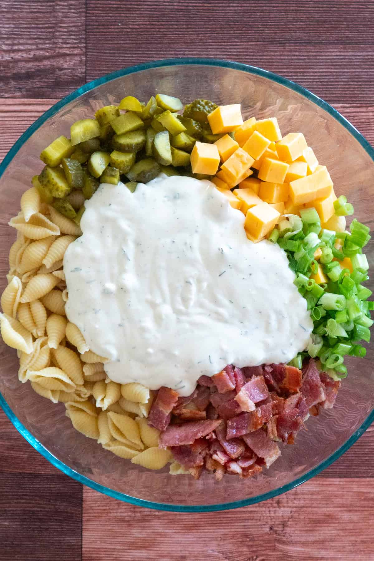 Prepared dressing pour over the top of pasta, dill pickles, cheese, green onions, and bacon.