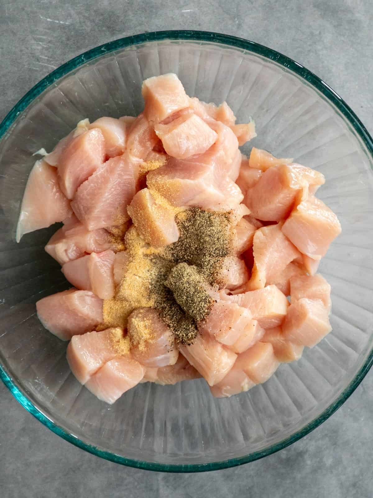 Cubed and seasoned chicken in a clear bowl.