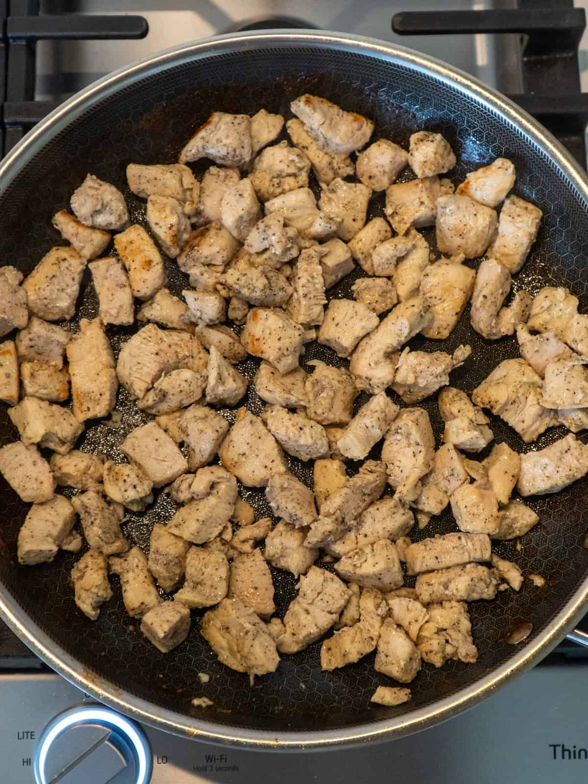 Cubed chicken breast being cooked in a skillet.