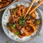 Teriyaki chicken and broccoli over a bowl of rice with chopsticks.