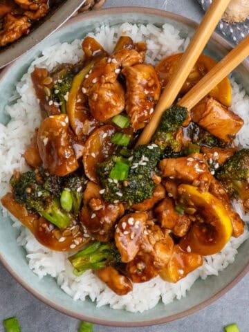 Teriyaki chicken and broccoli over a bowl of rice with chopsticks.
